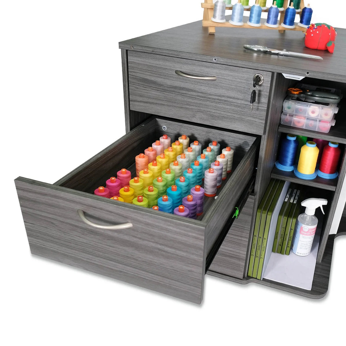 The Kangaroo Sydney Sewing Cabinet with Electric Lift by Arrow Companies, LLC features an open drawer filled with colorful thread spools and extra sewing supplies arranged on its shelves and tabletop.