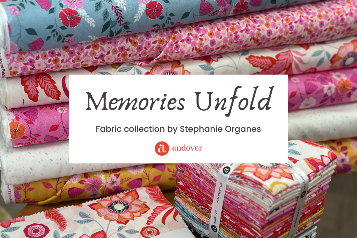 Stacks of colorful, floral-patterned fabrics surround a sign reading Memories Unfold: Fabric collection by Stephanie Organes with the Andover logo.