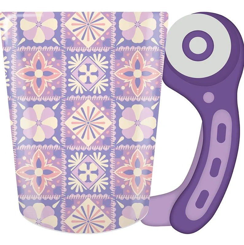 A purple mug with a handle shaped like a sewing rotary cutter, featuring a pastel pattern of pink and purple geometric flowers and squares.