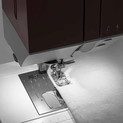 Close-up of the Quilted Joy Pfaff Quilt Ambition 635 Sewing and Quilting Machine stitching white fabric, showcasing the needle, presser foot, and sewing platform—ideal for quilting projects.