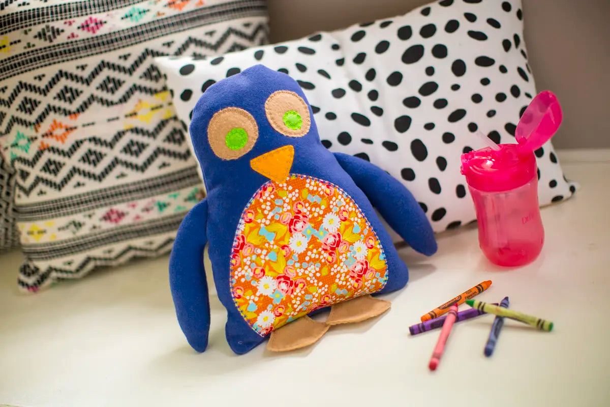 The Baby Lock Accomplish 2 Sewing Machine with FREE online sewing classes is displayed on a white surface, in front of black-and-white pillows, next to a pink sippy cup and several crayons.