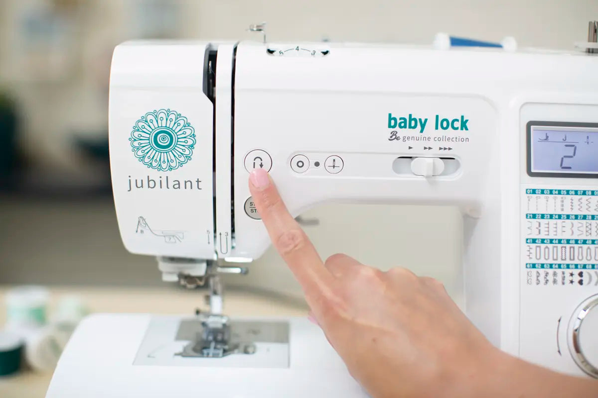 A hand presses a button on the Baby Lock Jubilant Sewing Machine, showing stitch options and a digital screen with the number 2.