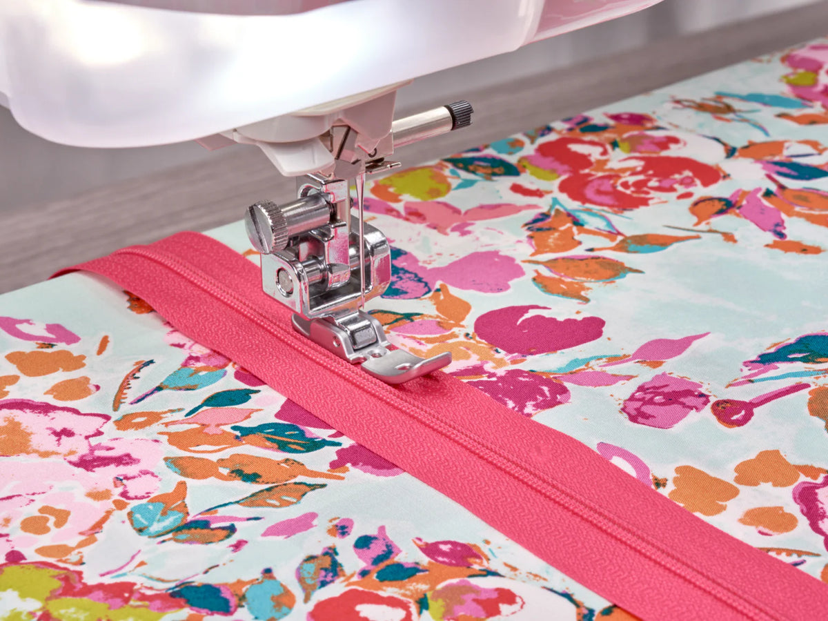 The Baby Lock Anthem Sewing & Quilting Machine with FREE 60 Days of Online Classes stitches a bright pink zipper onto floral fabric. Its StitchSync Regulation keeps the needle close to the edge, securing the zipper with precision.
