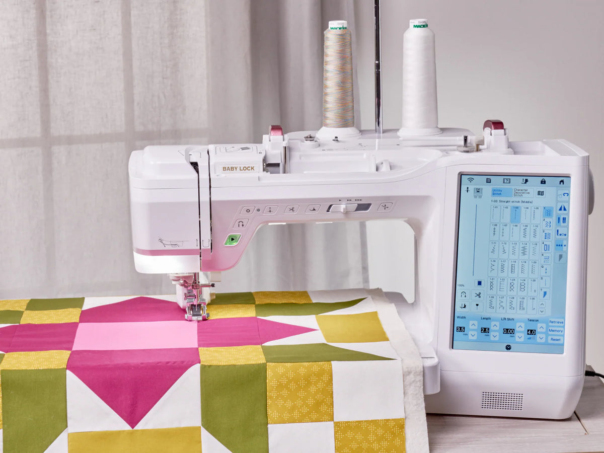 A Baby Lock Anthem Sewing & Quilting Machine with FREE 60 Days of Online Classes is stitching a quilt with pink, yellow, green, and white geometric patterns. Two large thread spools and a StitchSync Regulation touchscreen are visible.