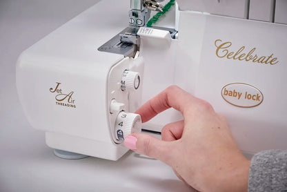 A hand adjusts the manual tension dial on a white Baby Lock Celebrate Serger Machine with Jet-Air Threading.
