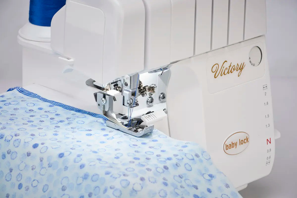 A close-up of the Baby Lock Victory Serger Machine with Jet-Air Threading, stitching blue and white patterned fabric using blue thread.