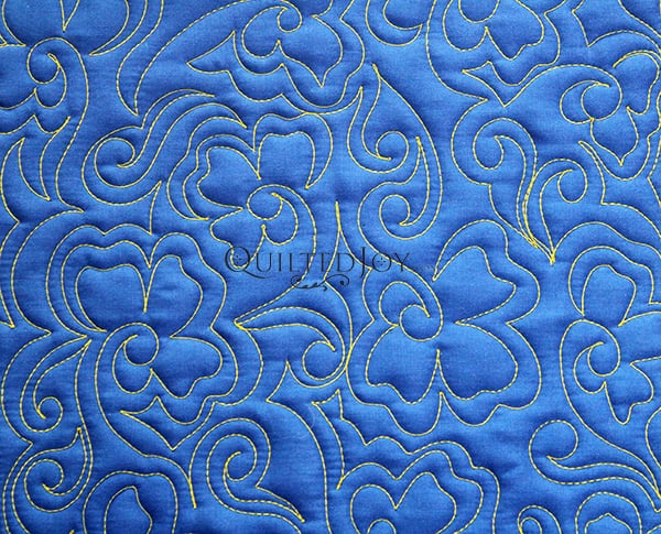 Blue fabric with an intricate quilted pattern of swirling yellow lines and floral shapes, creating a decorative and textured design.