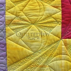Close-up of a colorful quilt with intricate machine-stitched patterns in yellow, purple, and red fabric sections. The stitching forms geometric shapes and curved lines. The word QUILTEDJOY is faintly visible on the yellow fabric.