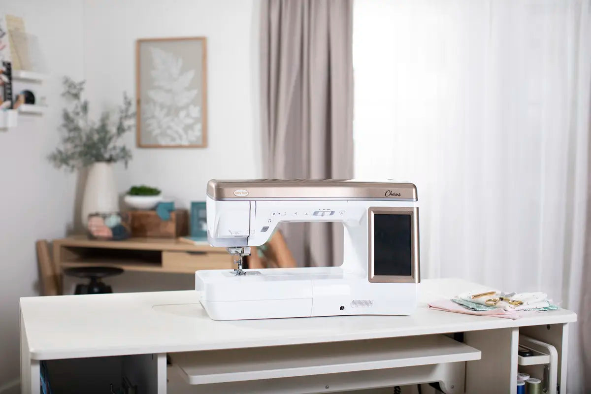 A Baby Lock Chorus Sewing Machine by Baby Lock rests on a white table in a bright, organized room with a desk, shelves, and a large window draped with sheer curtains.