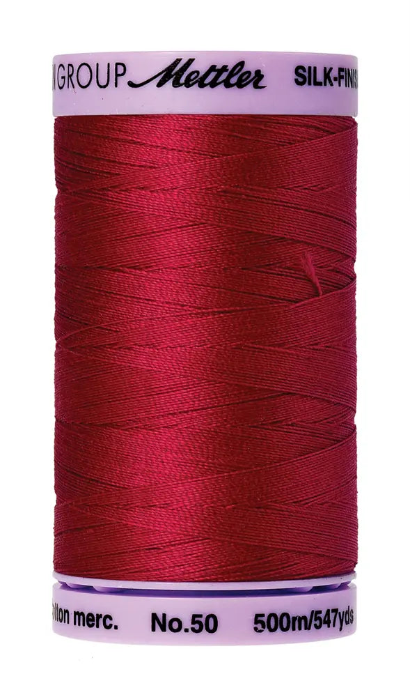 A spool of Mettler Cotton Silk Finish 50wt thread in Country Red, 500m/547yds, is shown against a white background.