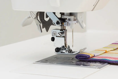The presser foot of the JUKI Kirei HZL-NX7 raised above layered pale fabric, showing the foot lift function at the needle.