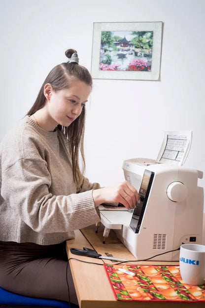 A quilter sitting at the JUKI Kirei HZL-NX7 in a bright sewing room, working at the machine with its extension table fitted.