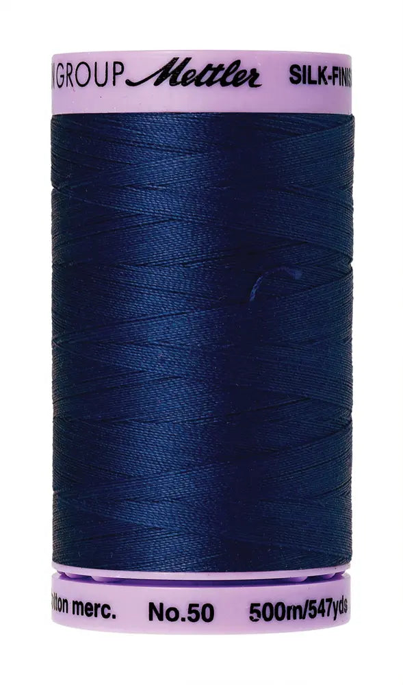 A spool of Mettler Cotton Silk Finish 50wt 500m in Imperial Blue with pink ends—ideal as a high-quality quilting thread.