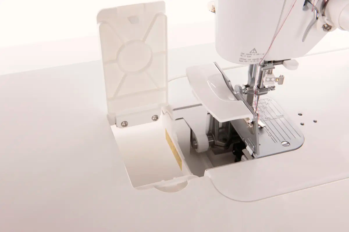 Close-up of an open JUKI TL-2000Qi Sewing and Quilting Machine showing the bobbin area and needle plate with the cover lifted, set against a plain background.