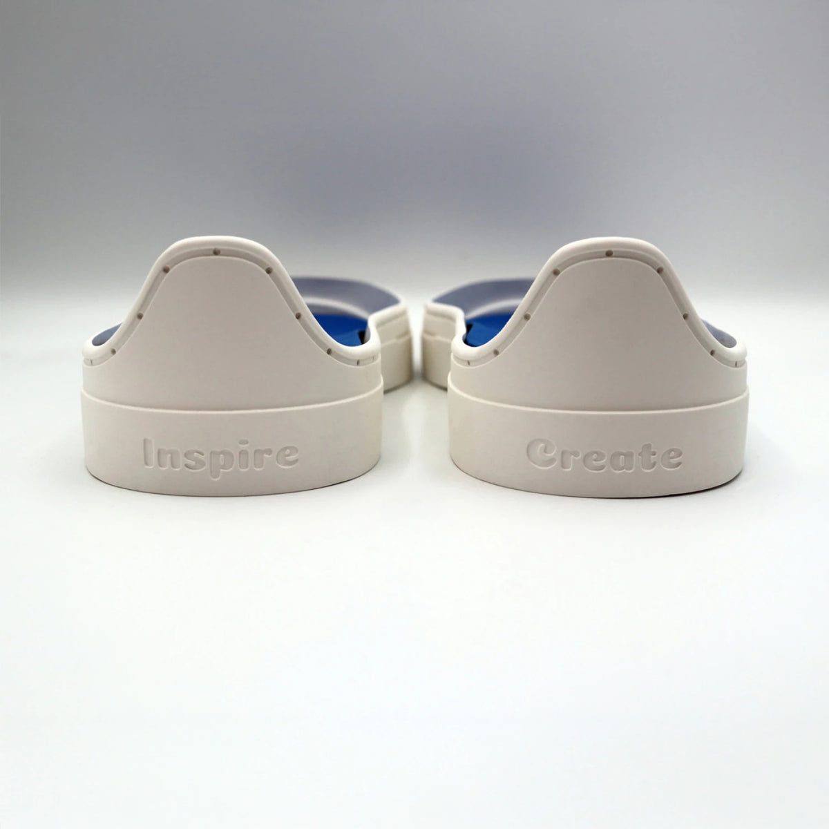 Two white plastic objects from the Patchwork Kicks White Shoe Kit by Checker Distributor sit side by side, labeled "Inspire" and "Create" in raised letters, resembling sneaker components on a white surface.