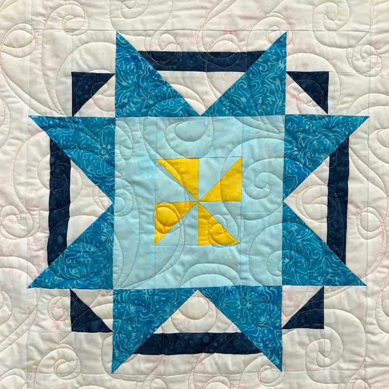 A quilt block featuring a central yellow and light blue pinwheel, surrounded by blue and teal star shapes with intricate stitching patterns on a white background.