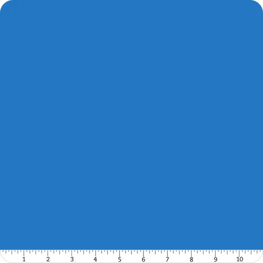 A square with rounded corners in solid blue, resembling Confetti Cotton™ Cobalt Solid Fabric Yardage by Riley Blake. A white ruler marked 1–10 inches lines the bottom, ideal for quilting cotton fabric projects.
