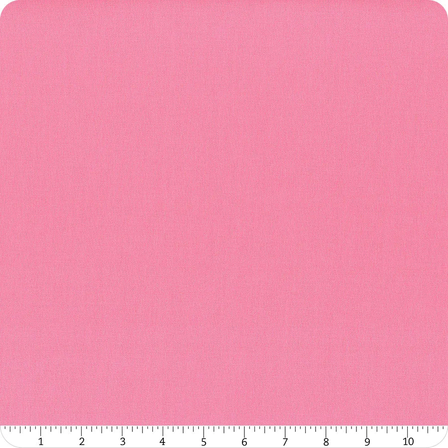 A square of Riley Blake's Confetti Cotton™ Piglet Pink Solid Fabric is shown on a white background, featuring subtle texture. A ruler at the bottom edge marks measurements from 0 to 10 inches.