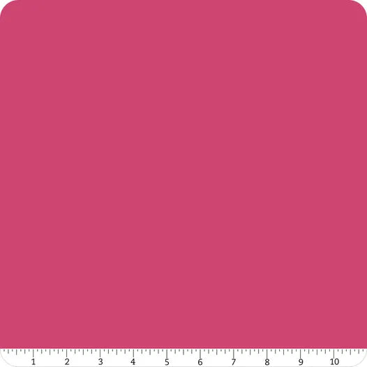 A square swatch of Confetti Cotton™ Riley Fuchsia Solid Fabric Yardage by Riley Blake with rounded corners. A white ruler marked 1 to 10 in black runs along the bottom edge for scale.