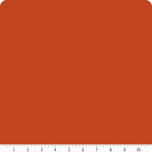 A square of solid reddish-brown fabric with rounded top corners. Along the bottom edge, a white ruler from 1 to 10 inches shows the scale of this Riley Blake Confetti Cotton™ Rusty Solid Fabric Yardage, perfect for quilting projects.