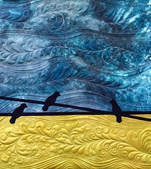 Quilt art featuring three black birds on a wire, with a swirling blue sky above and intricate yellow patterns below, resembling a landscape with textured clouds and fields.