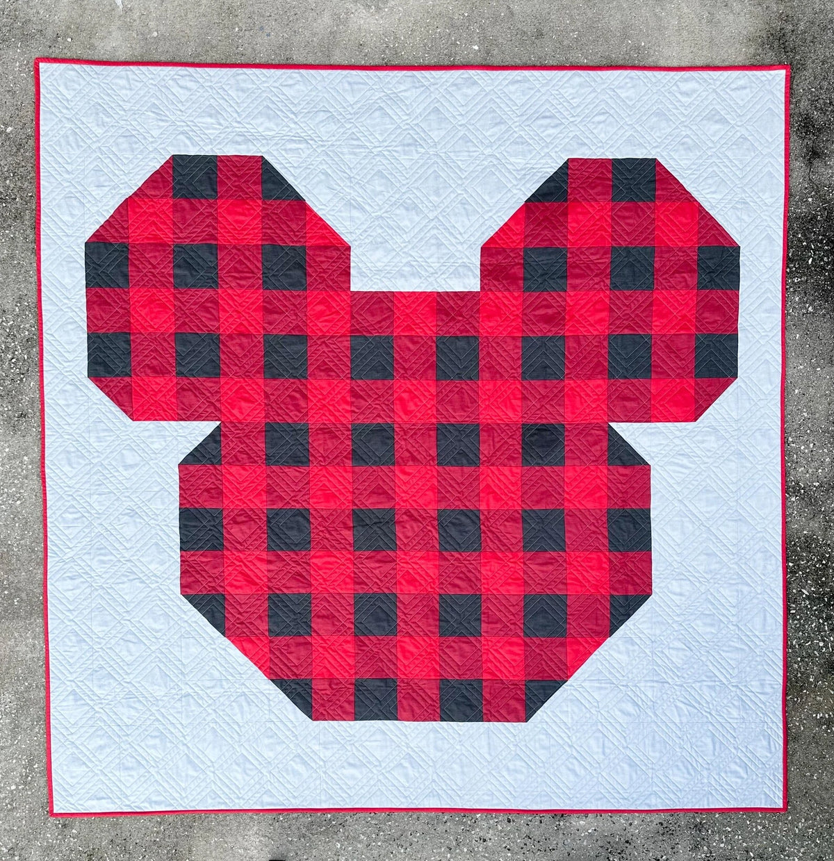 Quilt with red and black checkered pattern shaped like a heart on a concrete surface