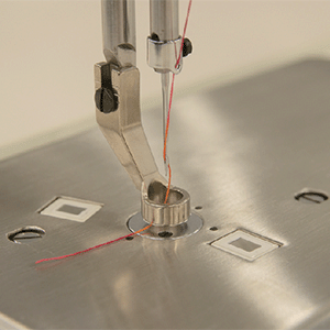A close view of the needle and hopping foot of the JUKI Miyabi J-350QVP on the machine bed, with red thread running through the needle.