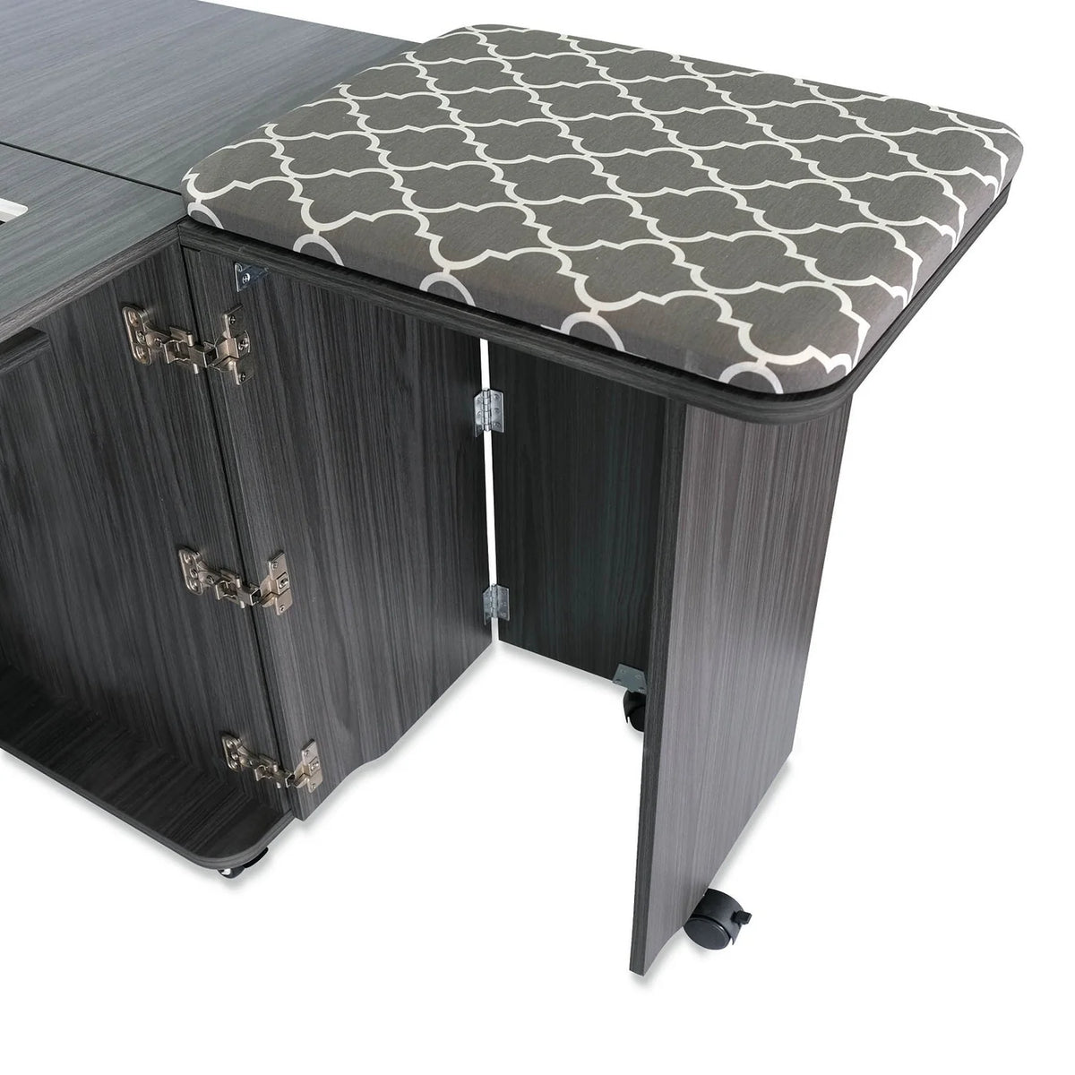 A cushioned stool with a gray and white geometric pattern is partially tucked under the Arrow Companies, LLC Kangaroo Sydney Sewing Cabinet with Electric Lift, which features multiple hinges and caster wheels.