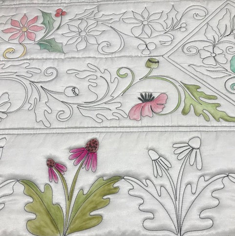 A quilted fabric with intricate floral patterns, some flowers and leaves partially colored in shades of green, pink, and red, while others remain outlined in black on a white background.